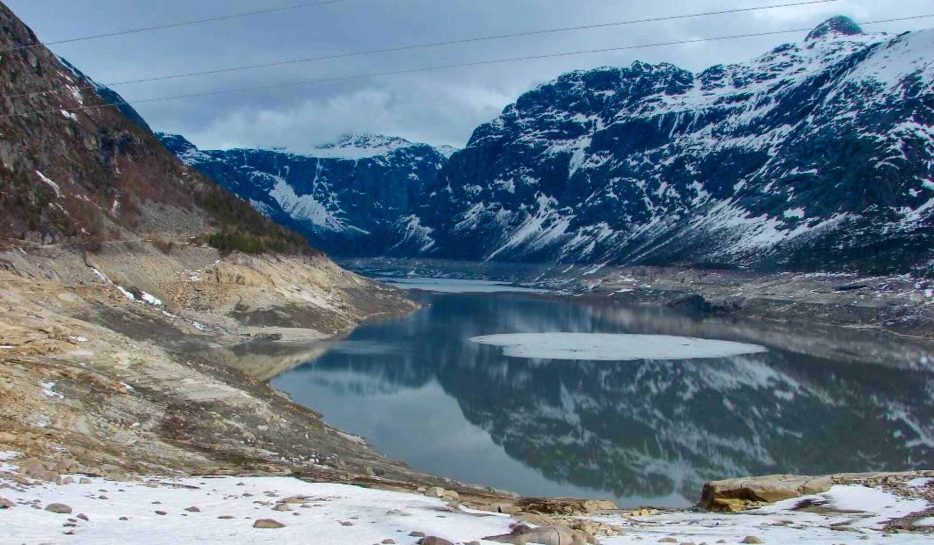 Fjellvann med lav vannstand, mellom snøkledde fjell